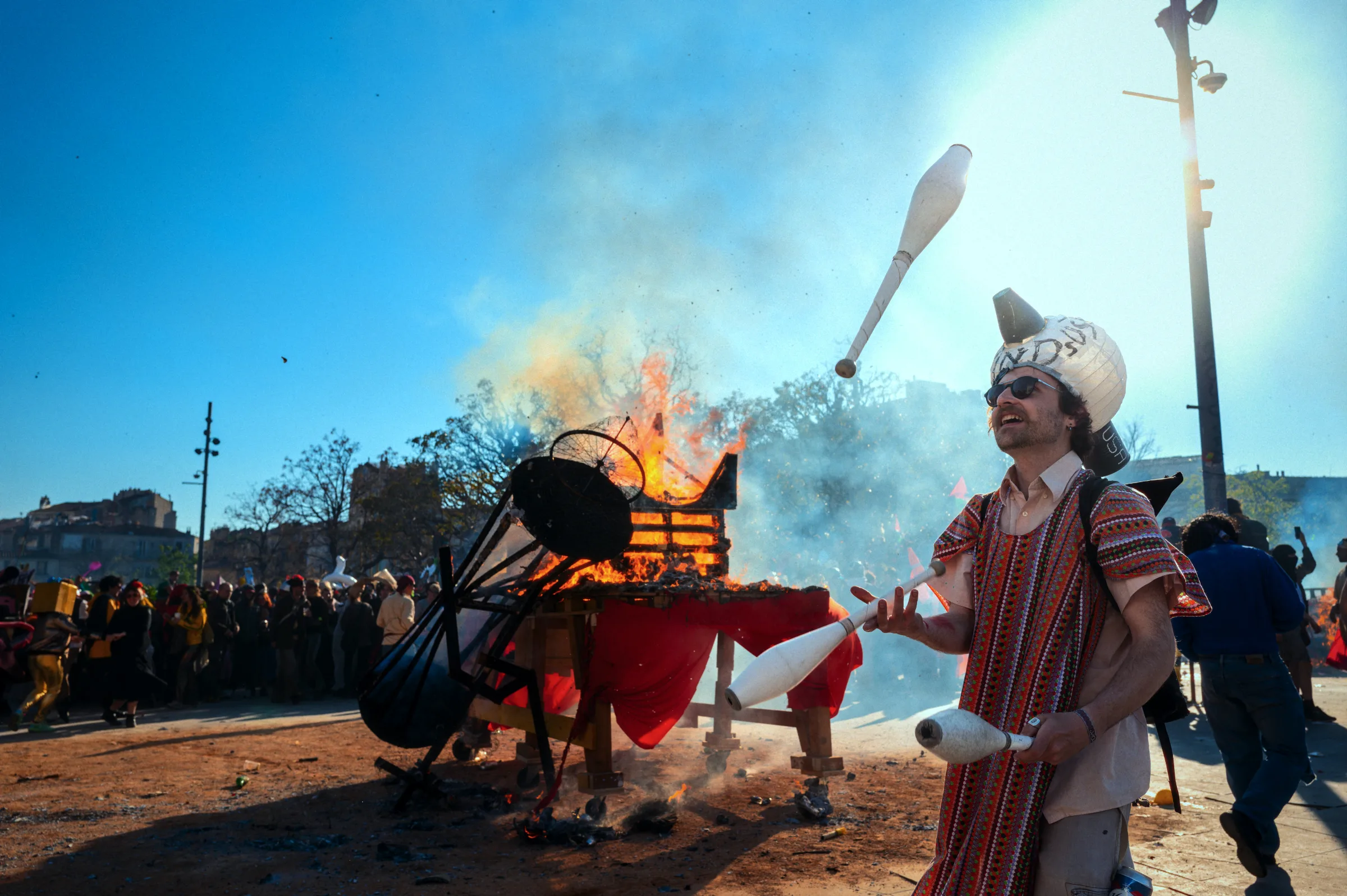 Un jongleur costumé lance des massues devant le bûcher du Caramantran en flammes, lors du carnaval de la Plaine à Marseille.