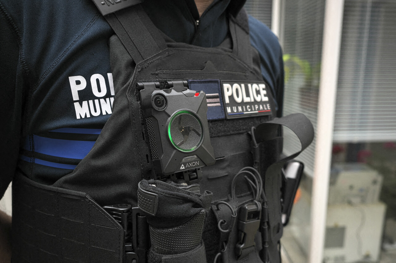 Un policier en tenue avec une caméra corporelle fixée sur son gilet, portant des équipements de sécurité.