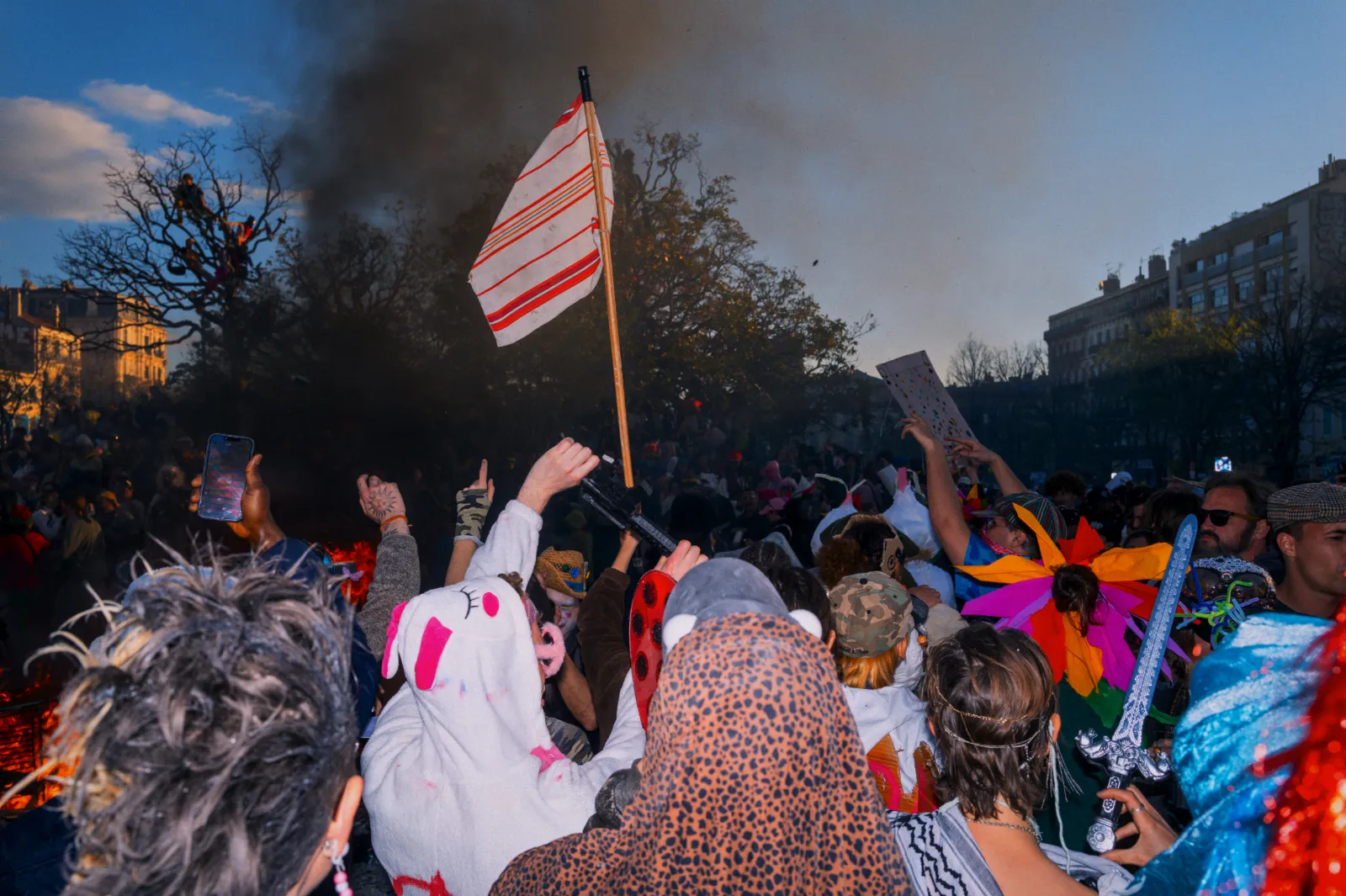 Foule festive au Carnaval de la Plaine, Marseille, avec costumes colorés, drapeaux et ambiance animée sous un ciel bleu.