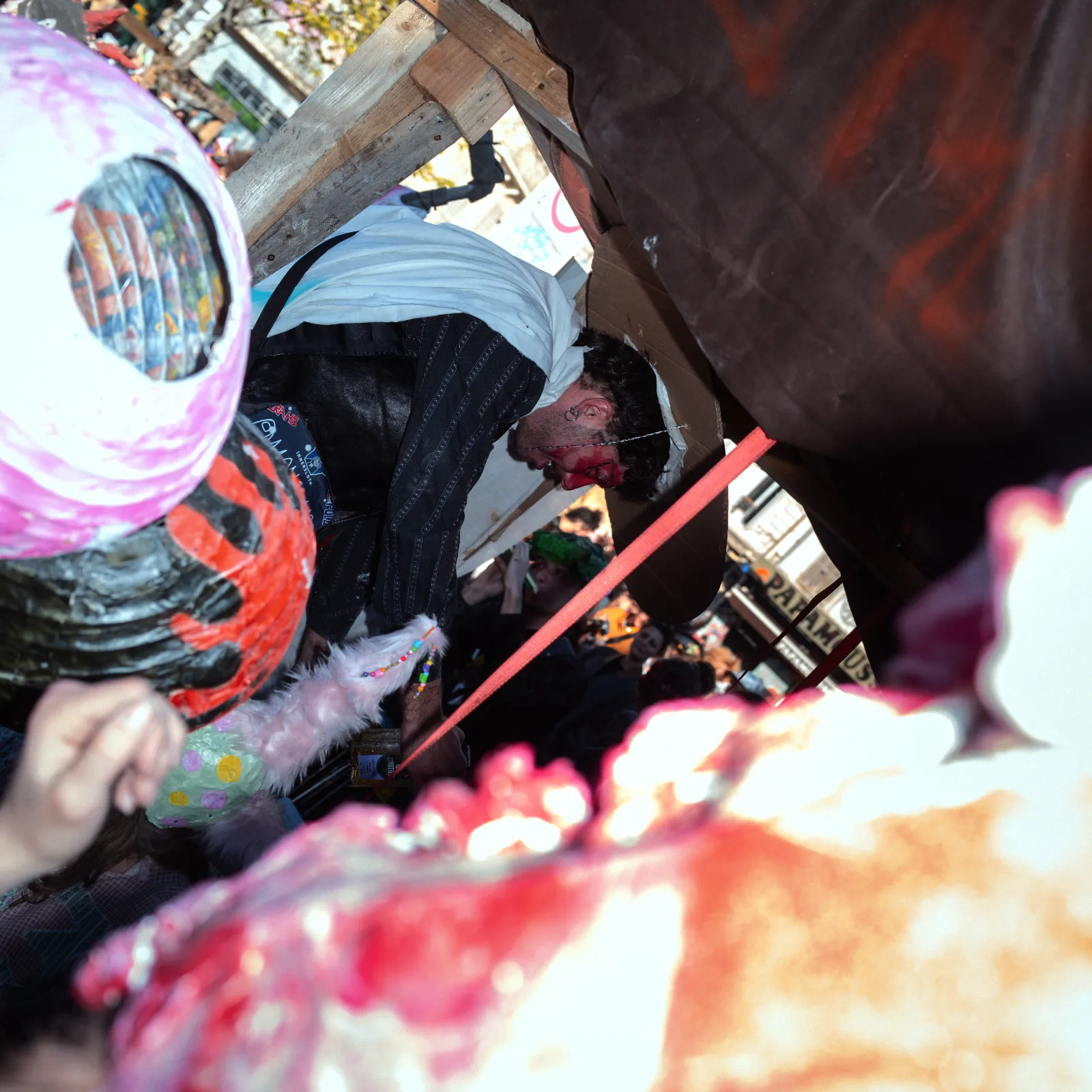 Un homme en costume est aspergé d'eau, entouré de participants au carnaval avec des masques colorés et des décorations festives.