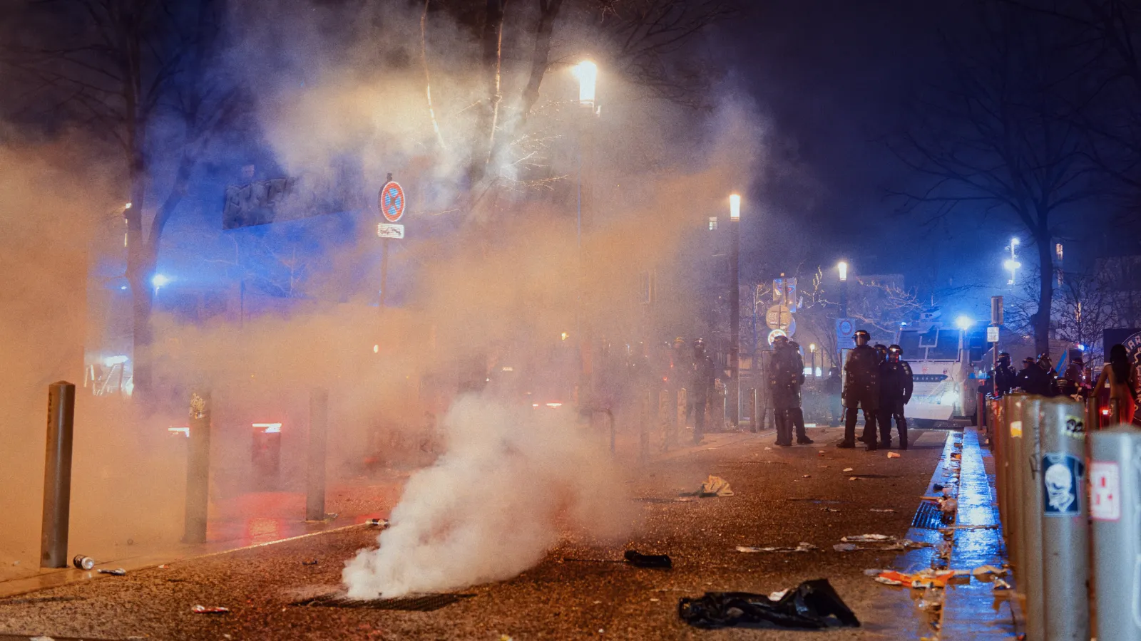 Atmosphère nocturne du Carnaval de la Plaine, avec des fumigènes, des policiers en arrière-plan et des débris au sol.