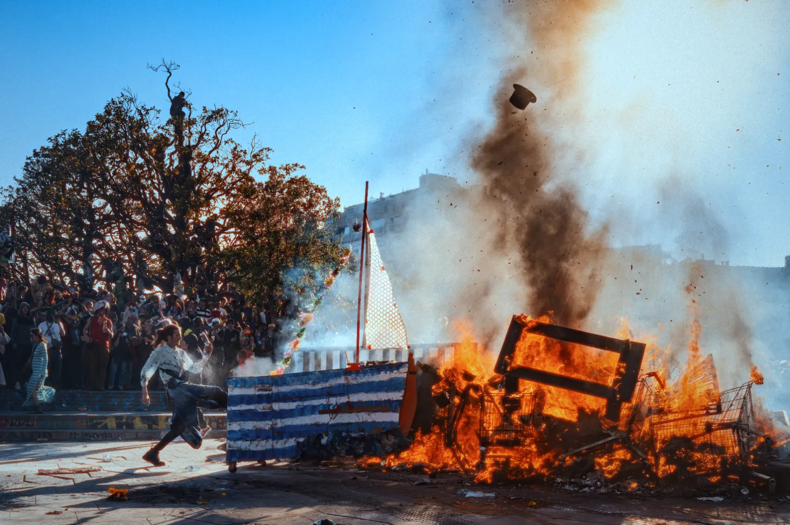 Un homme court près d'un feu de joie au Carnaval de la Plaine, entouré de spectateurs, avec des flammes et des débris en arrière-plan.