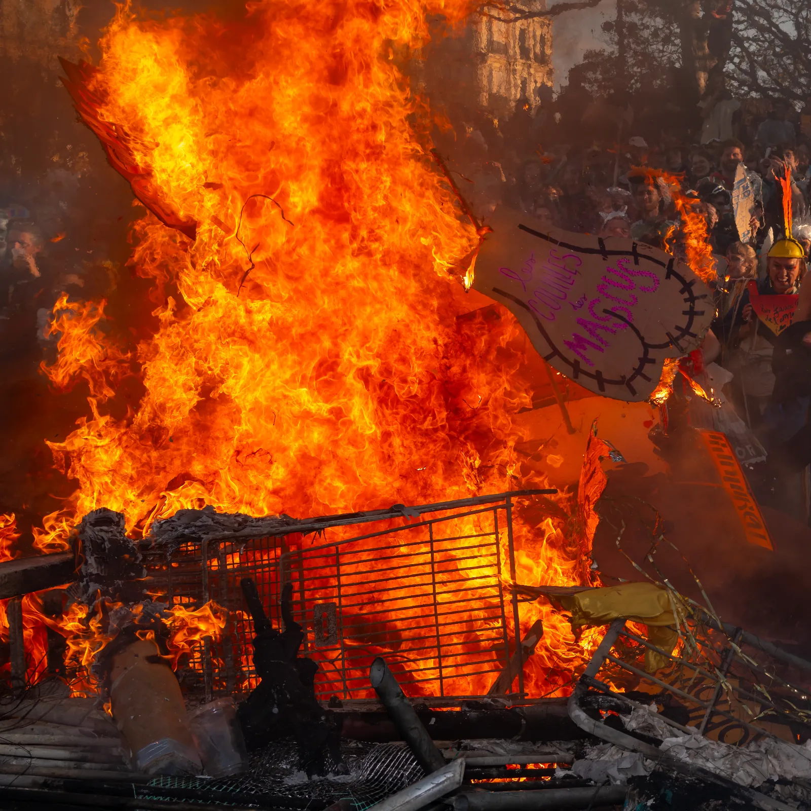 Flammes intenses d'un grand feu de carnaval, avec des débris enflammés et des spectateurs en arrière-plan, lors du Carnaval de la Plaine.