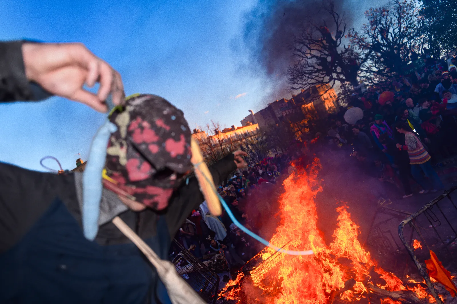 Un participant masqué danse près d'un grand feu, entouré d'une foule festive au Carnaval de la Plaine à Marseille.