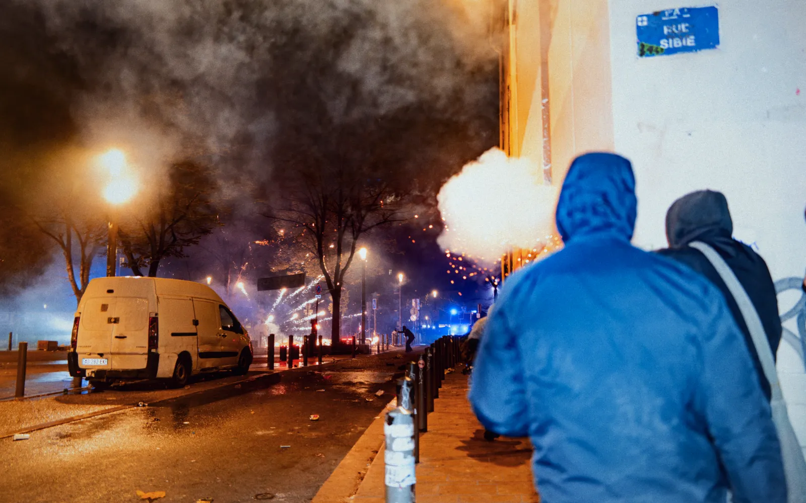 Scène nocturne du Carnaval de la Plaine, Marseille, avec des fumigènes et des lumières, des personnes marchant sur une rue animée.